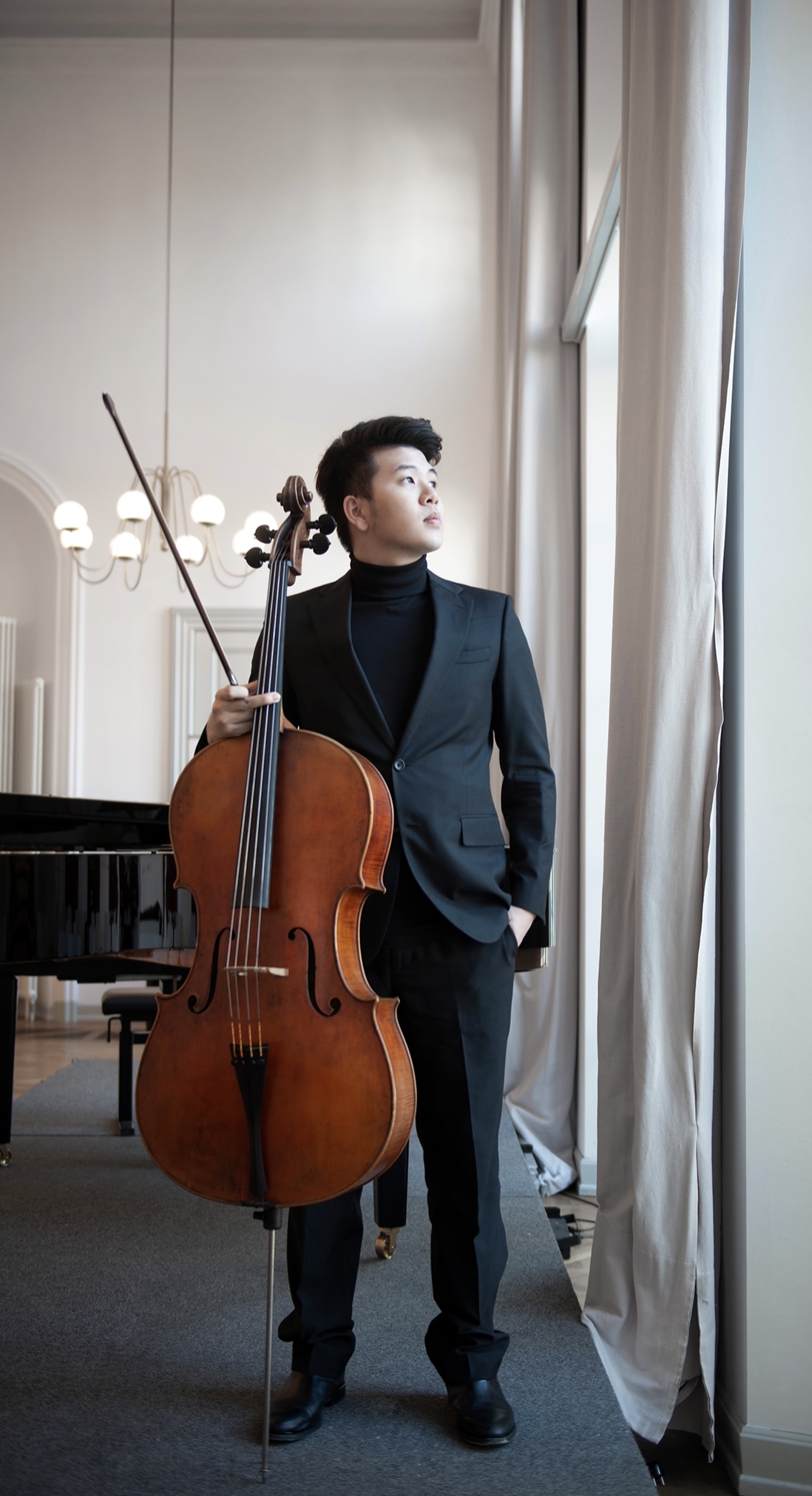 Yun Ho standing with his cello and bow beside a sunlit window