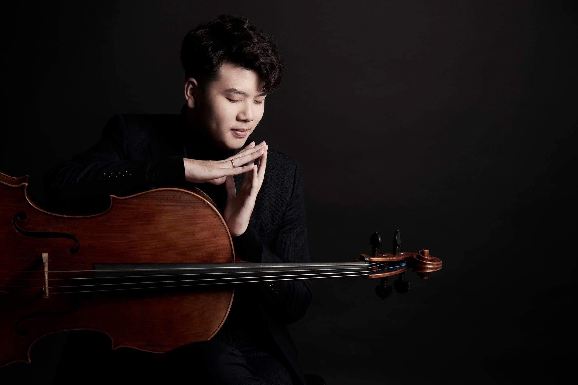 Yun Ho leaning over his cello in a dark studio portrait